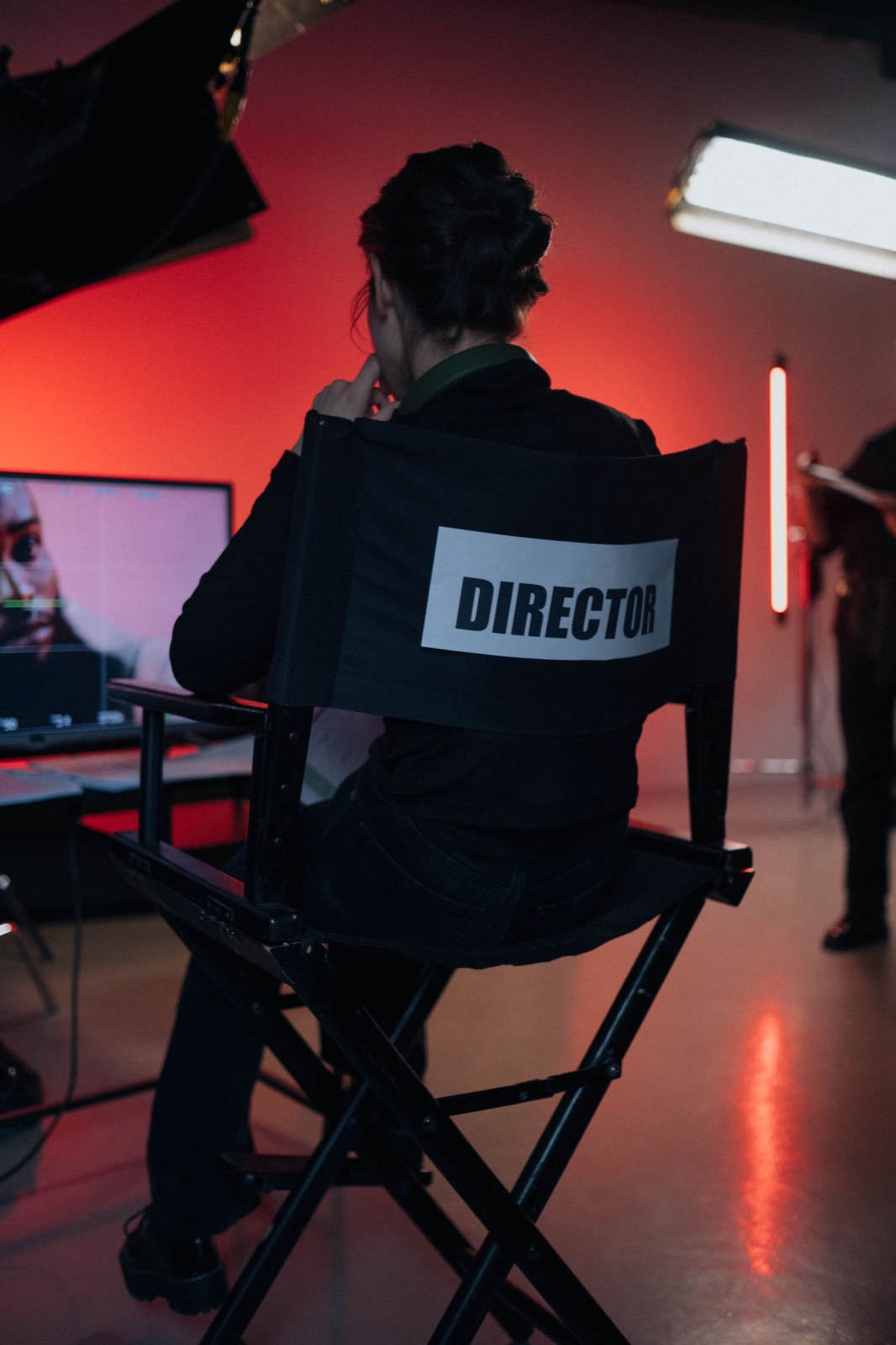A director seated in a director's chair in front of a monitor on a red-lit set