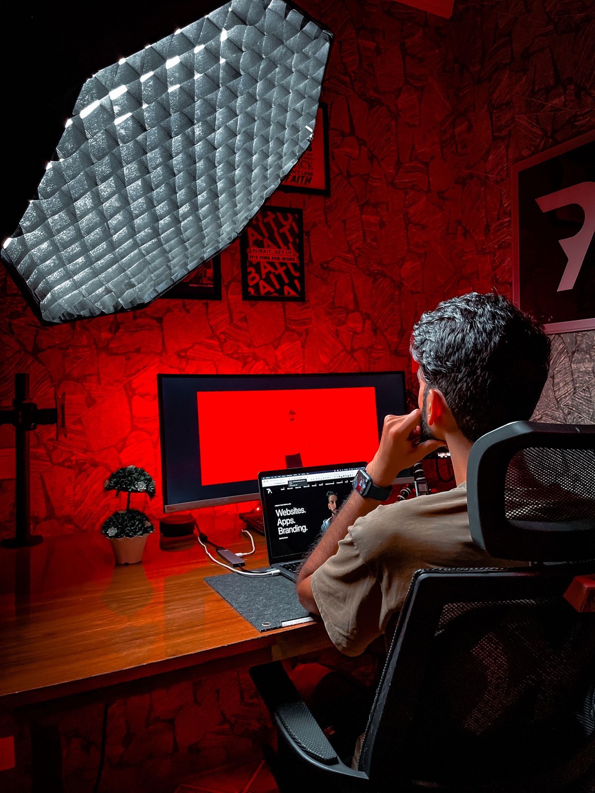 A designer at a desk lit in red, with a laptop open to a branding website